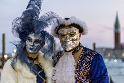 Couple wearing masks and costumes in city during sunset