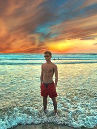Full length of shirtless man standing in sea during sunset