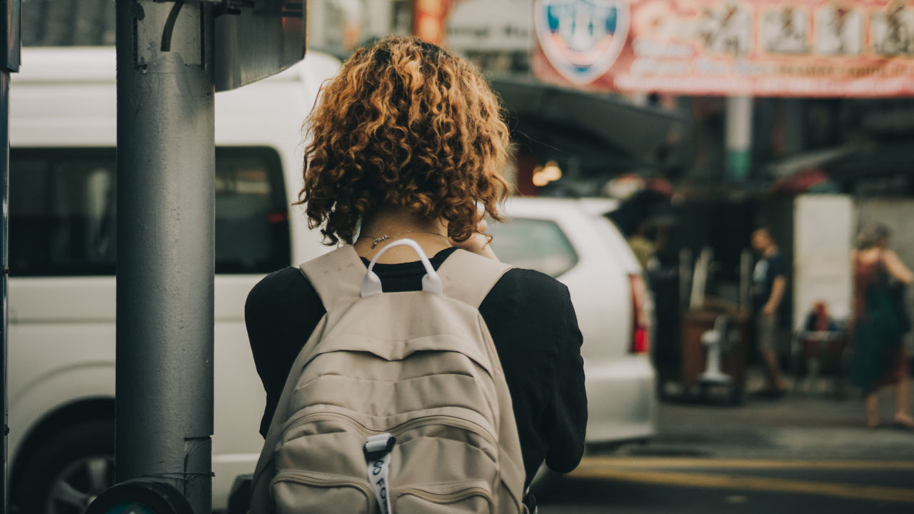 one person, rear view, focus on foreground, real people, hair, transportation, hairstyle, women, travel, mode of transportation, lifestyles, city, standing, incidental people, portrait, curly hair, architecture, public transportation, adult, outdoors