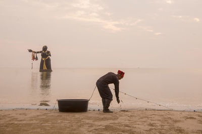 Men standing on beach against sky during sunset