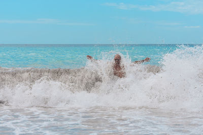 Man with arms outstretched swimming in sea against sky
