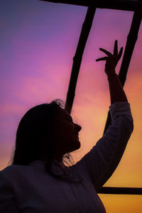 Portrait of silhouette woman with arms raised against sky during sunset