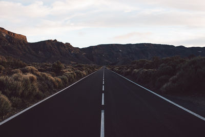 Road leading towards mountains against sky