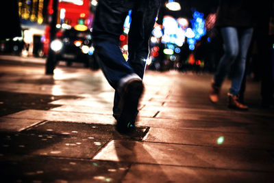 Low section of people walking on sidewalk in city at night