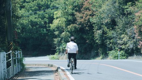 Rear view of person riding bicycle on road