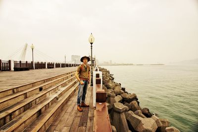 Rear view of man standing on pier over sea against sky