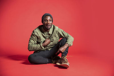 Portrait of young man sitting against red background