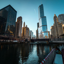 Modern buildings by river against sky in city