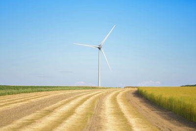 Windmills on field against clear blue sky