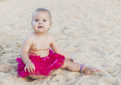 Portrait of cute girl sitting on sand at beach