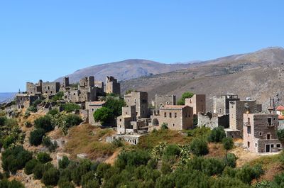 Old buildings on field by mountain against blue sky