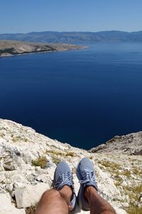 Low section of man sitting on mountain against sea