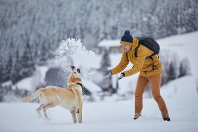 Full length of man throwing snow on dog during winter