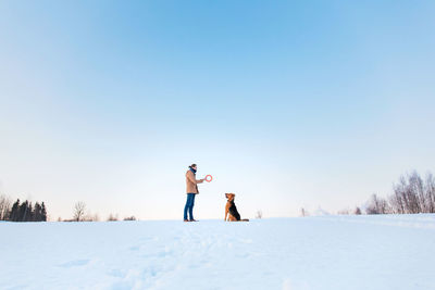 People standing on snow covered field against clear sky