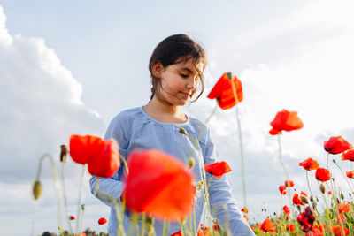 Low angle view girl standing in the field of poppies on a sunny day