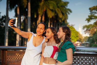 Tourists taking a selfie at a bridge on the cali river boulevard with la ermita church on background