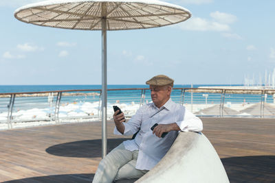 Rear view of man using mobile phone at sea against sky