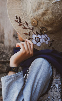 Young woman hiding face with hat against wall