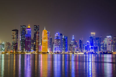 Illuminated modern buildings in city against sky at night