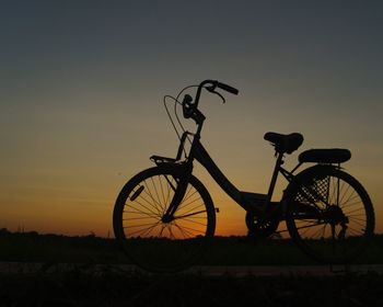 Silhouette bicycle parked on field against sky during sunset