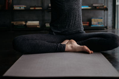 Low section of woman practicing yoga on mat at home