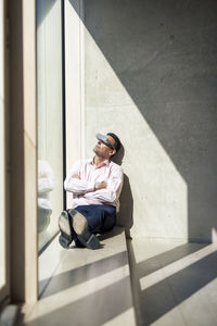 Mature businessman watching through futuristic glasses sitting on window sill in office