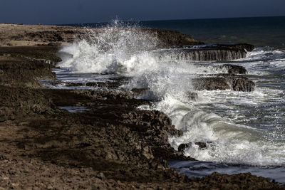 Water splashing on rocks by sea against sky