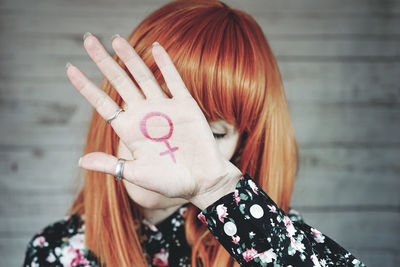 Mid adult woman showing gender equality sign while standing against wall