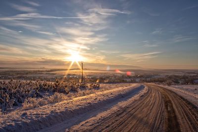 Tire tracks on snow covered field against sky during sunset