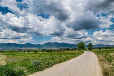 Road passing through field against cloudy sky