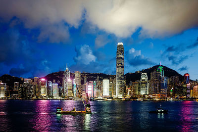 Illuminated buildings by river against sky at night