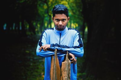 Portrait of young man standing by wooden post against trees in forest