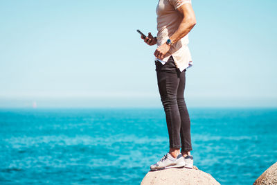 Low section of woman standing on sea shore against sky