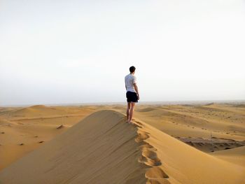 Rear view of man standing on sand dune at desert