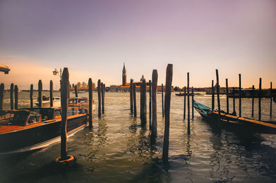 Gondolas amidst wooden posts in grand canal against sky