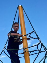 Low angle view of boy on swing against clear blue sky