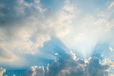 Low angle view of sunlight streaming through clouds