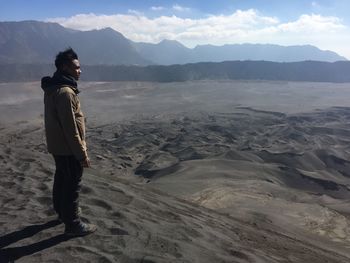 Side view of man standing on sand dune in desert against mountains
