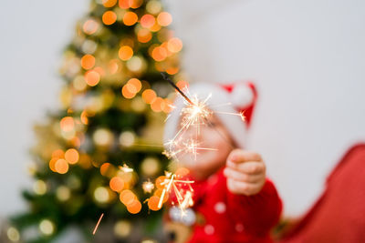 Close-up of boy holding burning sparkler by christmas tree