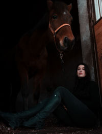 Woman sitting with horse at stable