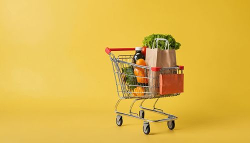 Close-up of miniature shopping cart against yellow background