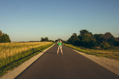 Rear view of man walking on road against clear sky