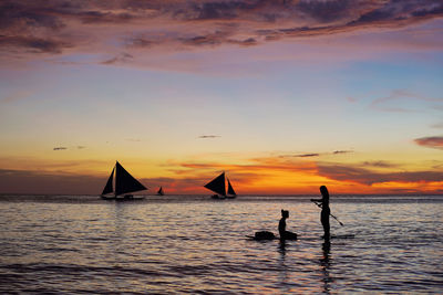 Silhouette people on sea against sky during sunset