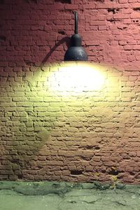 Close-up of illuminated lamp on brick wall