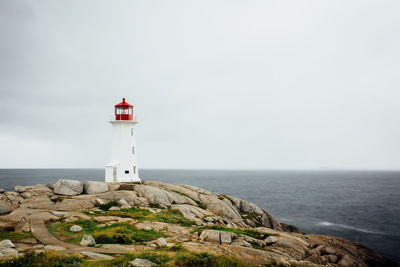 Lighthouse on rock by sea against sky