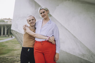 Portrait of smiling non-binary friends standing against wall at park