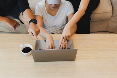 Group of friends working on laptop with hand pointing at screen in living room.