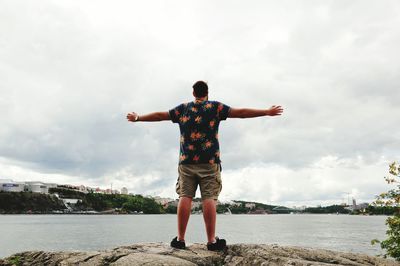 Rear view of man standing by river with arms outstretched