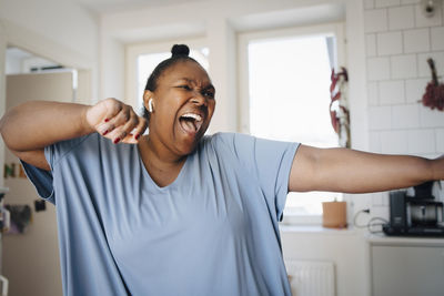 Joyful woman dancing while listening music in kitchen at home