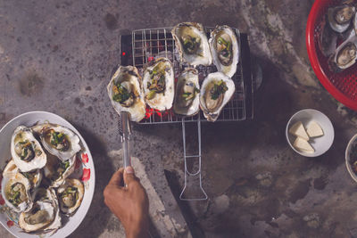 Cropped hand of man making mussels on barbecue grill at home